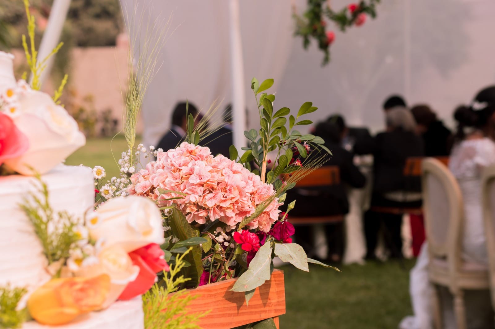 Arreglo floral y pastel de boda con fondo de personas en un evento en Cieneguilla