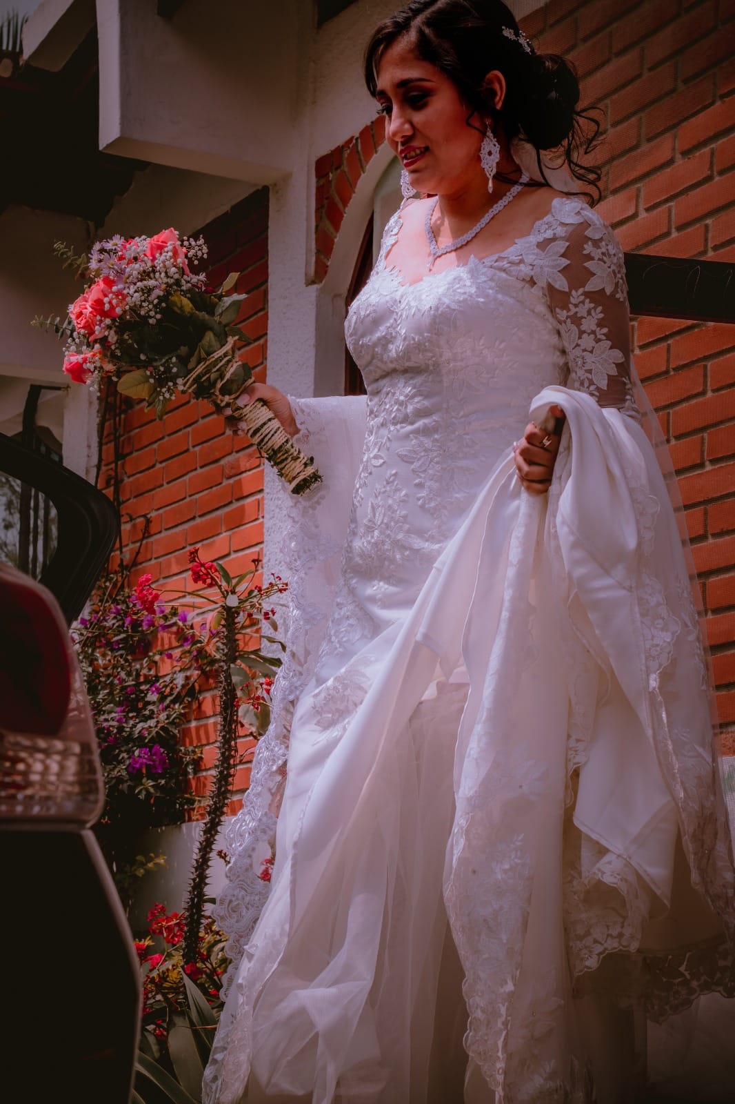 Novia levantando su vestido de encaje floral mientras sostiene un ramo de flores en una boda en Cieneguilla