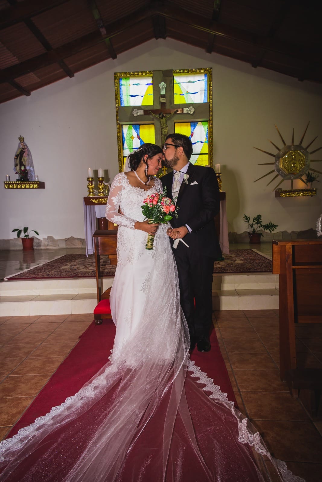 Pareja de novios en traje oscuro y vestido blanco dentro de una capilla en Cieneguilla