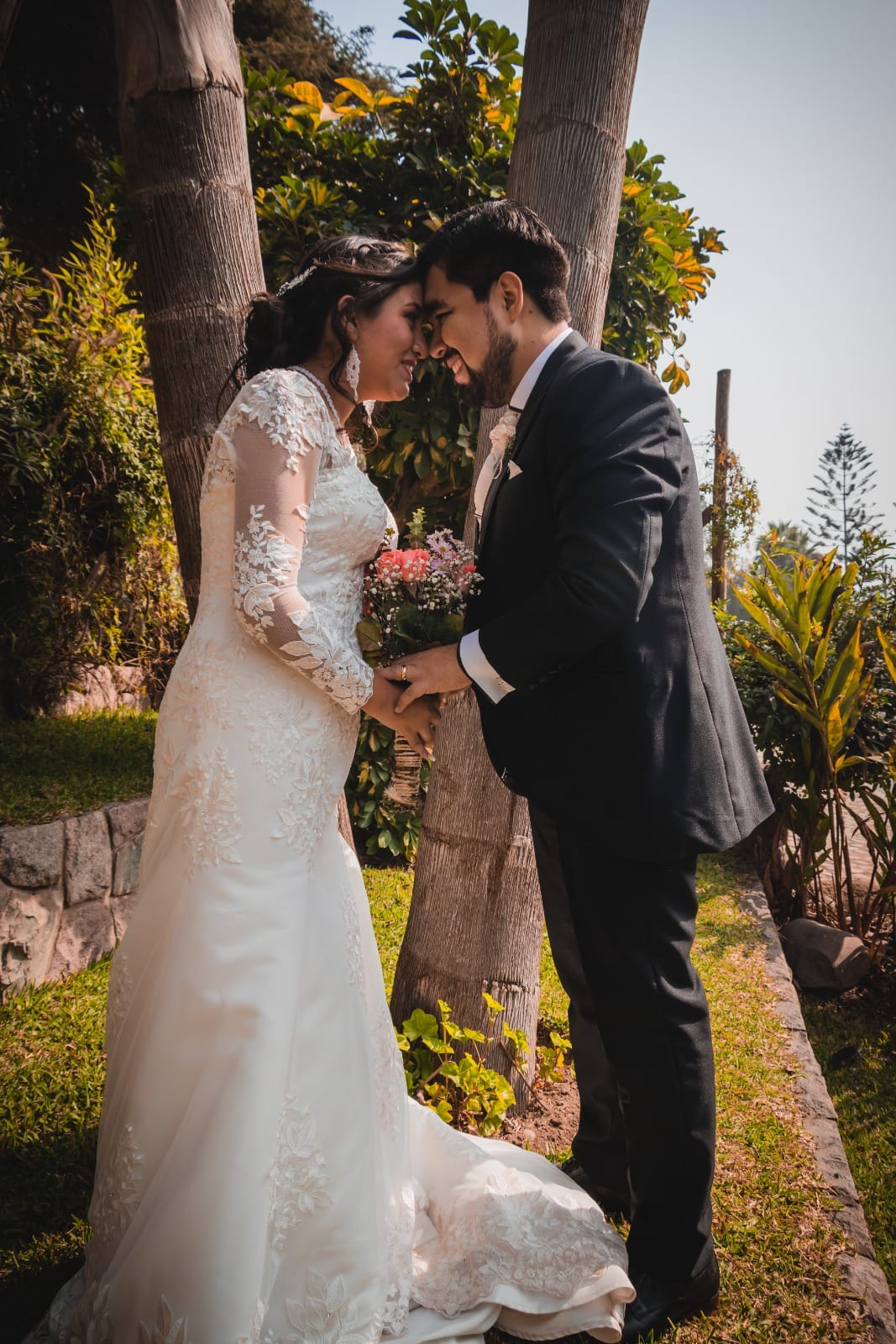 Pareja de novios con traje oscuro y vestido blanco en un jardín en Cieneguilla