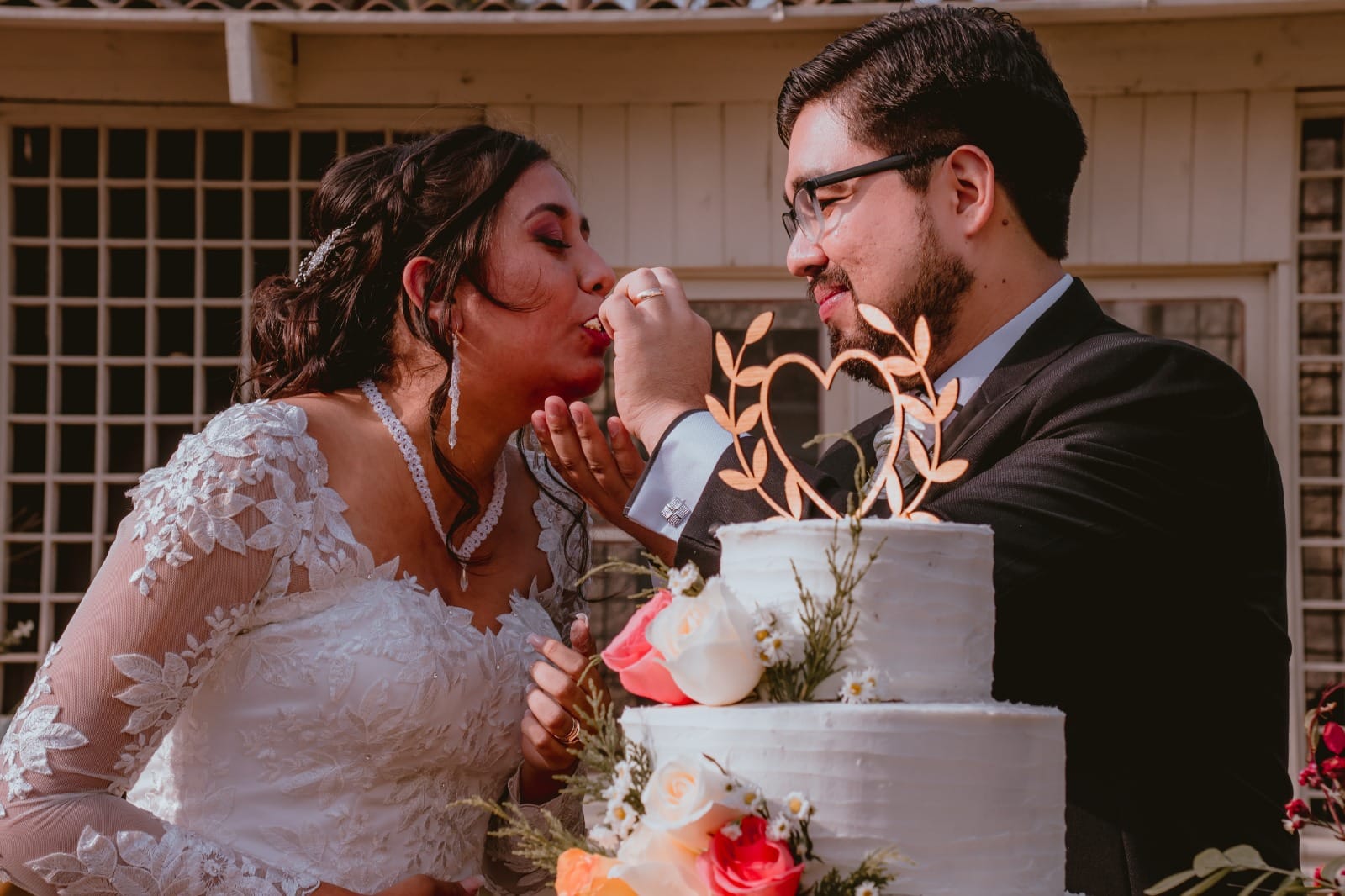 Pareja de novios en traje oscuro y vestido blanco cortando el pastel de bodas en Cieneguilla