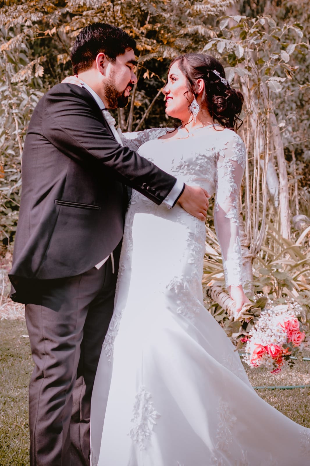 Pareja en traje oscuro y vestido blanco sosteniendo un ramo de flores en una boda en Cieneguilla