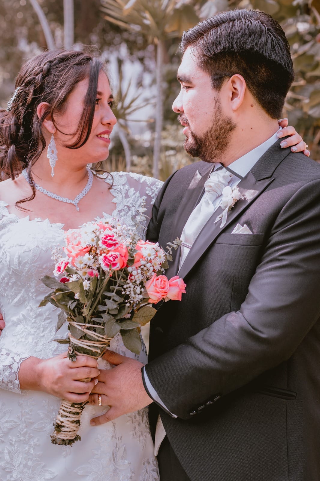 Pareja de novios con traje oscuro y vestido blanco, sosteniendo un ramo de flores en una boda al aire libre en Cieneguilla