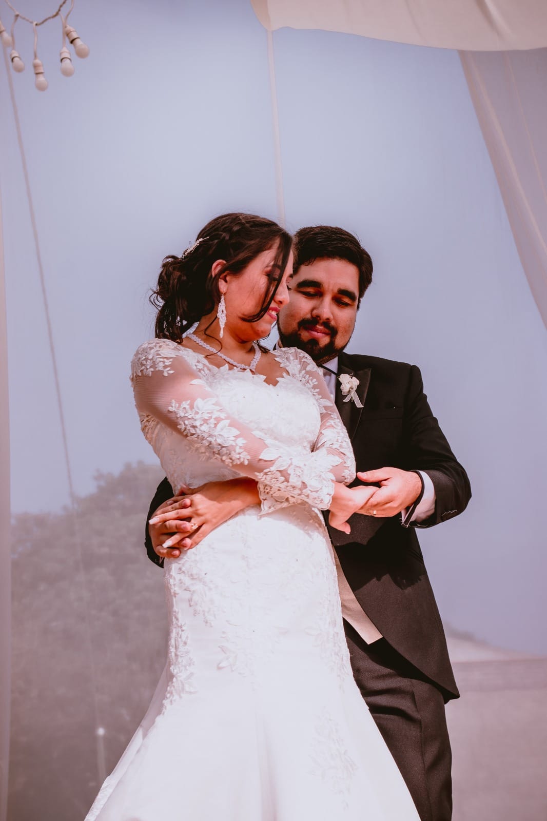Pareja en traje oscuro y vestido blanco con encaje en una boda al aire libre en Cieneguilla