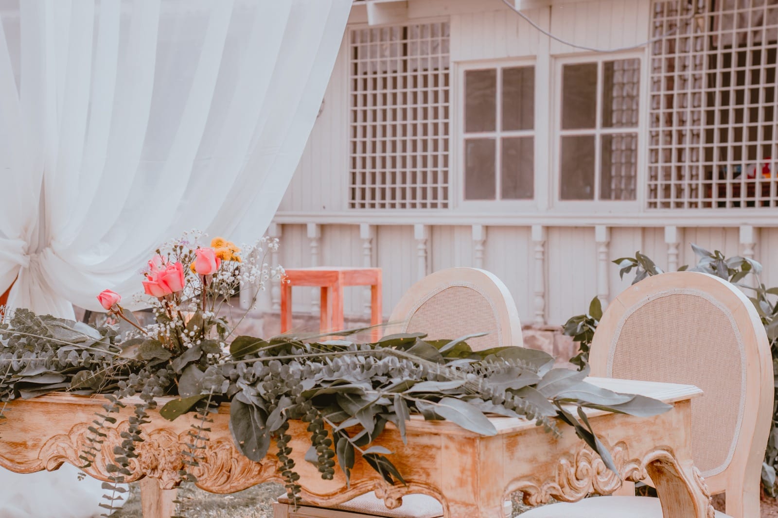 Pareja de novios en traje oscuro y vestido de encaje blanco sentados en una mesa decorada con flores y vegetación en Cieneguilla