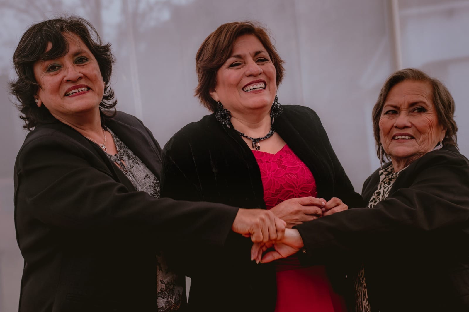 Tres personas vestidas de manera formal, con sus rostros ocultos, tomadas de la mano en un entorno interior