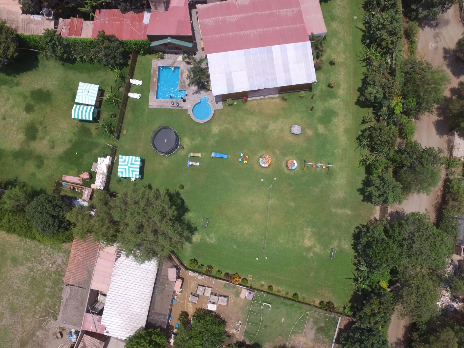 Vista aérea de un área recreativa con piscina, jacuzzi, césped, trampolín, área de juegos infantiles y mobiliario de exterior en una casa en alquiler en Cieneguilla.