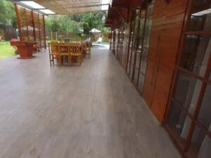 Comedor exterior rústico en una casa en alquiler en Cieneguilla con mesas y sillas de madera, sofás marrones y decoración vegetal.