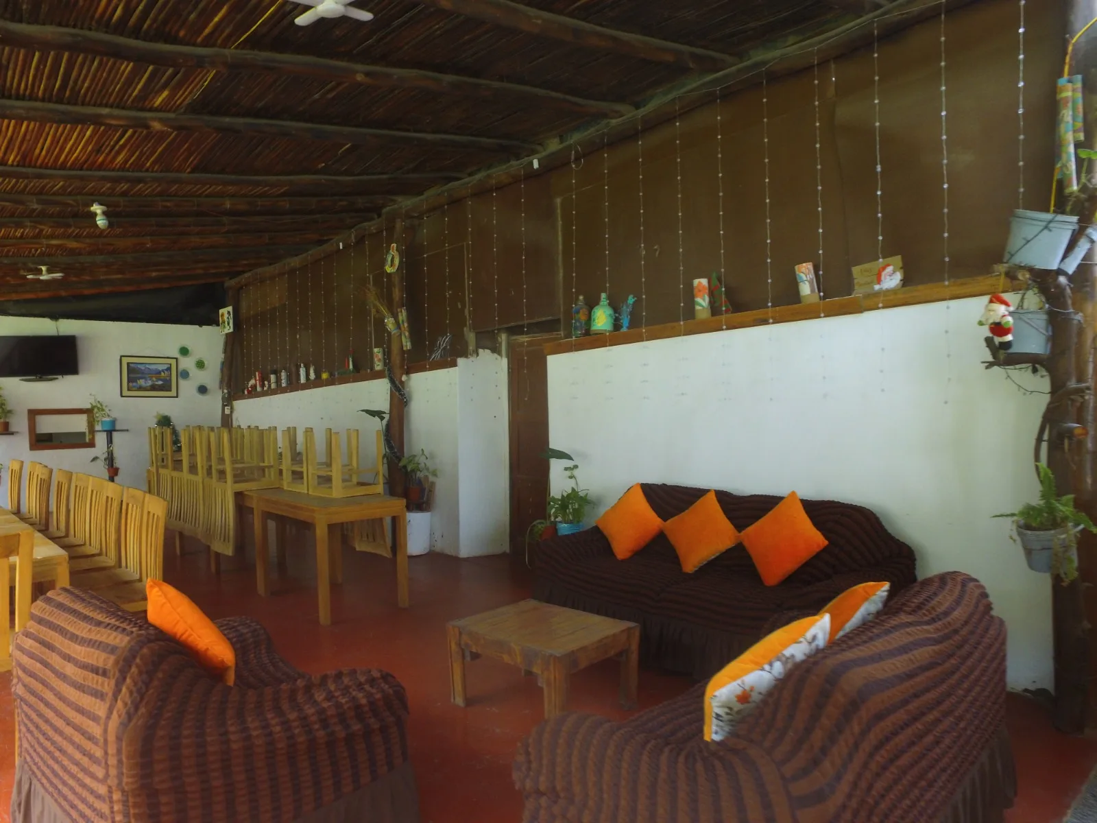 Comedor exterior rústico en una casa en alquiler en Cieneguilla con mesas y sillas de madera, sofás marrones y decoración vegetal.