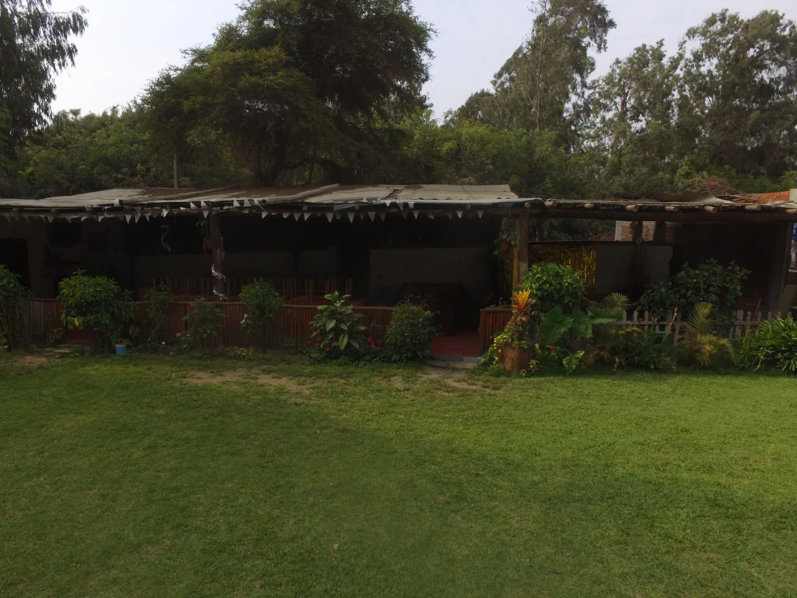 Comedor exterior rústico en una casa en alquiler en Cieneguilla con mesas y sillas de madera, sofás marrones y decoración vegetal.