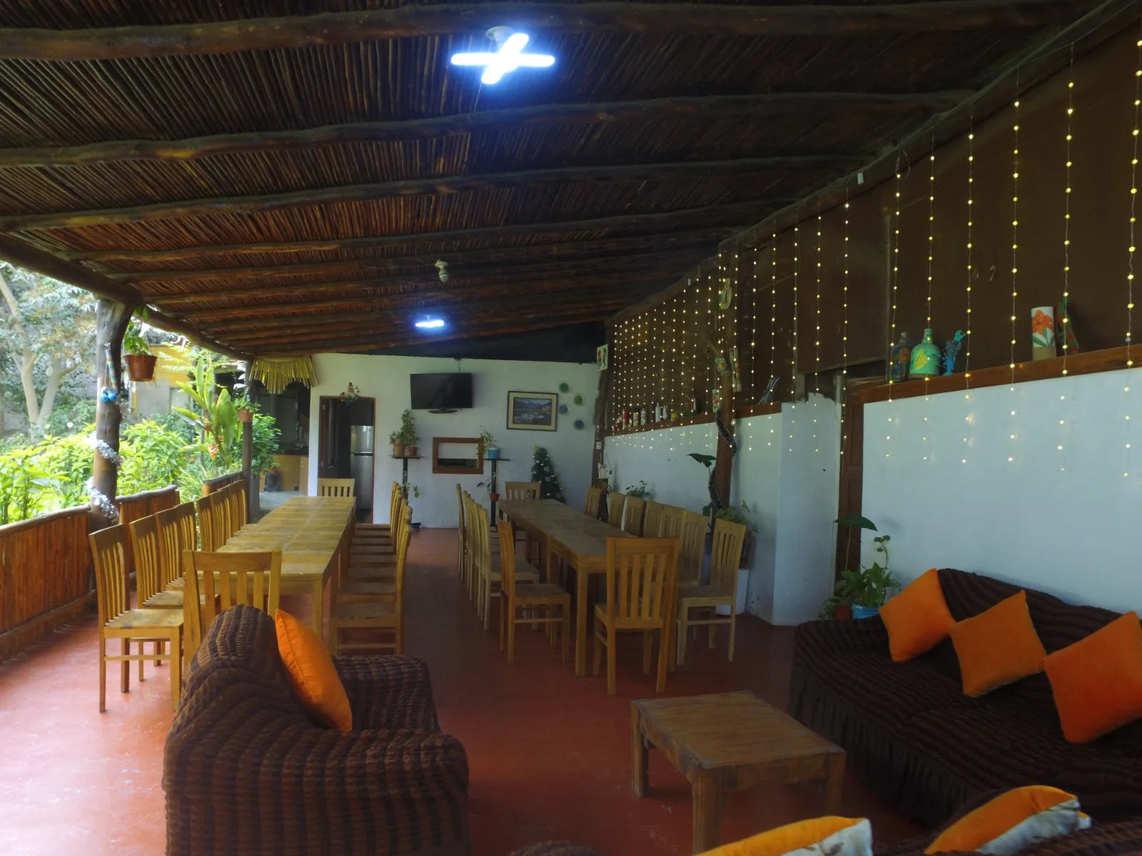 Comedor exterior rústico en una casa en alquiler en Cieneguilla con mesas y sillas de madera, sofás marrones y decoración vegetal.