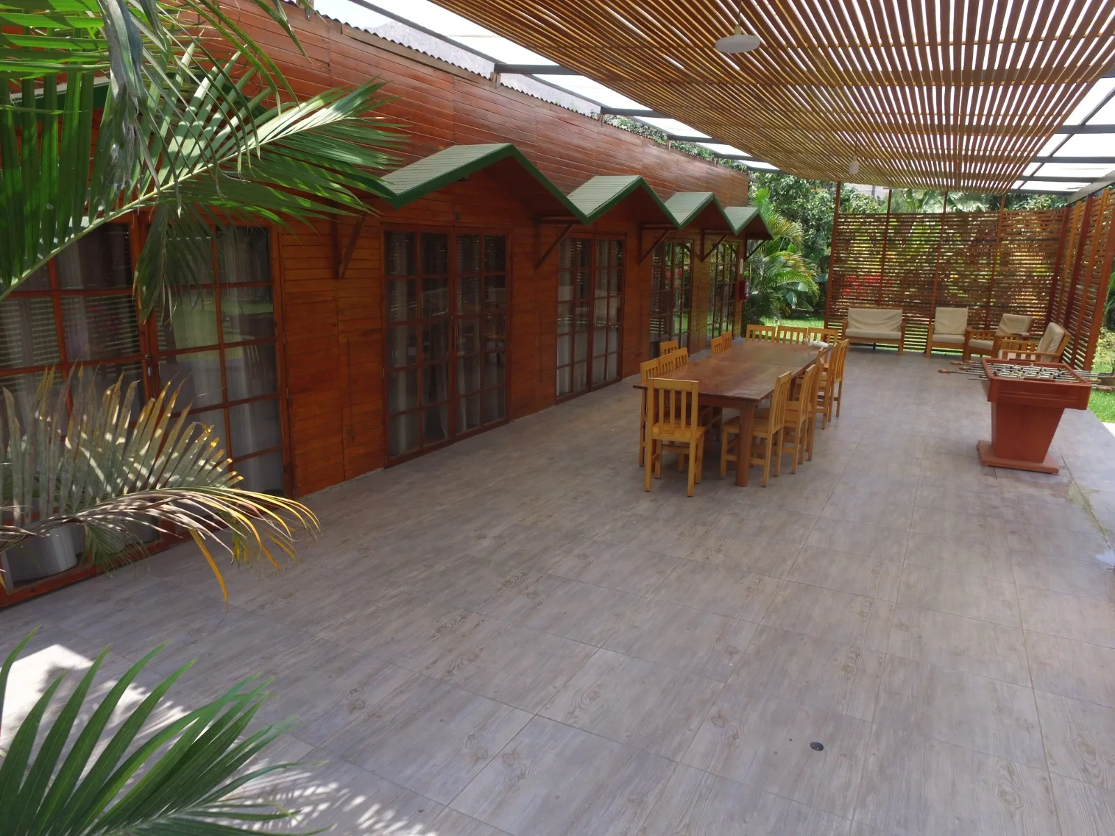 Comedor exterior rústico en una casa en alquiler en Cieneguilla con mesas y sillas de madera, sofás marrones y decoración vegetal.