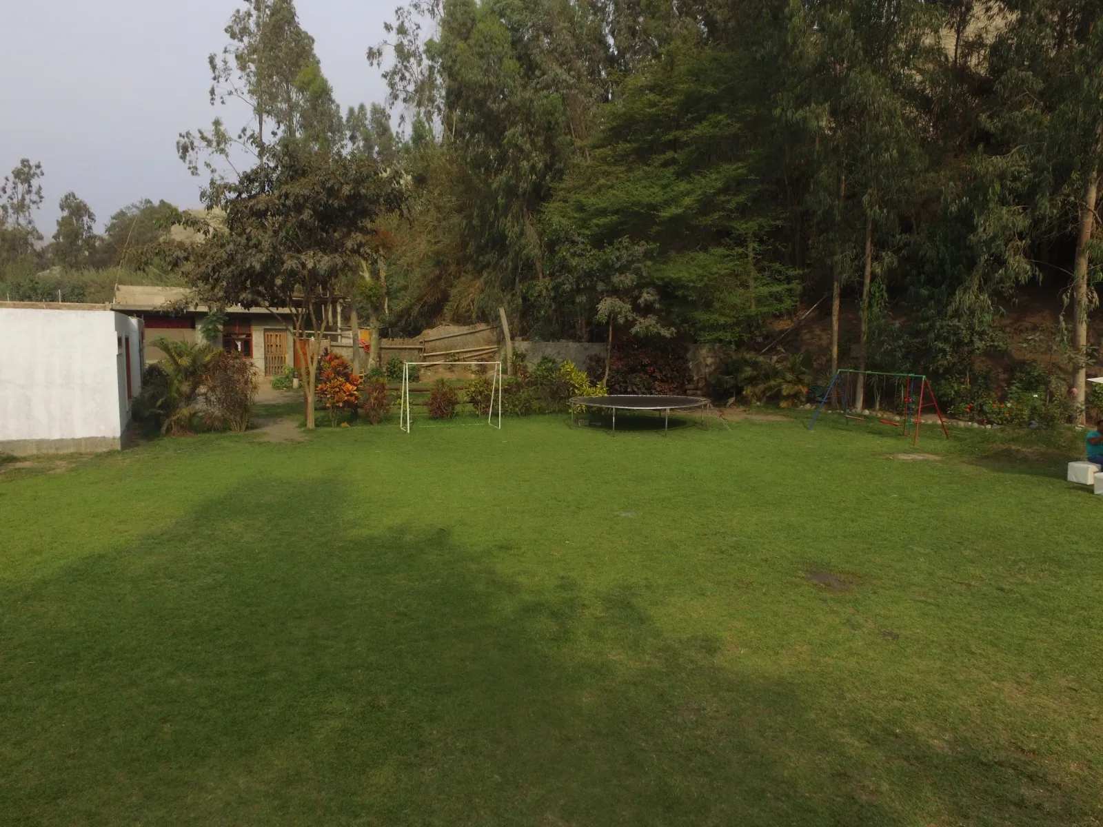 Área de jardín trasero en Cieneguilla con césped bien cuidado, juegos infantiles y vegetación.