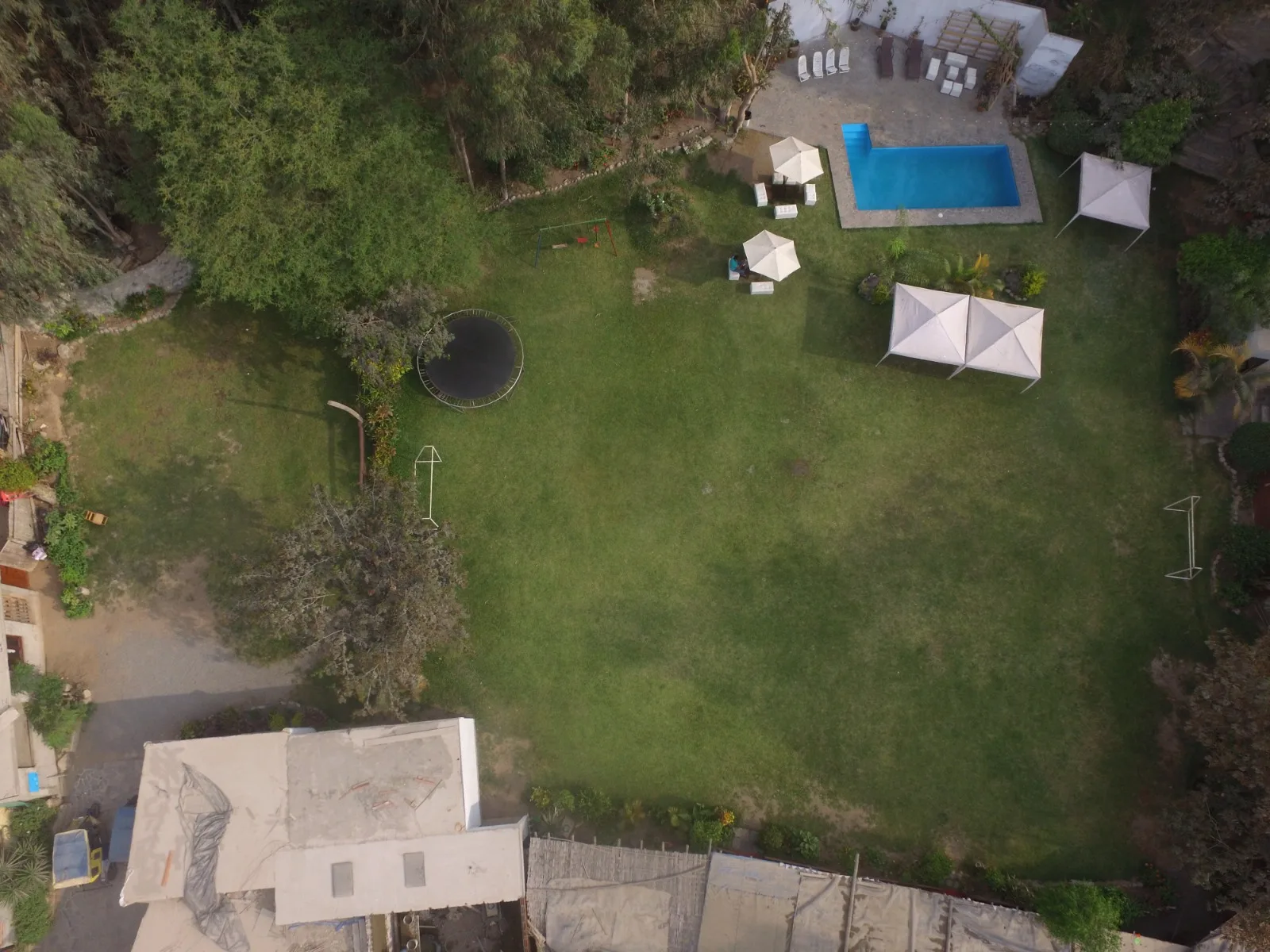 Vista aérea de un jardín trasero grande con piscina, carpas blancas, trampolín y área de juegos en una casa en alquiler en Cieneguilla.