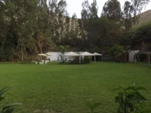 Patio exterior con césped, toldos blancos, sillas y mesas, columpios y una portería de fútbol en una casa en alquiler en Cieneguilla.