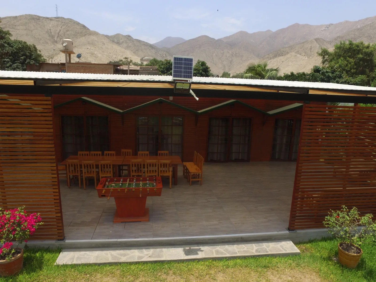 Patio exterior con estructura de madera, mesa larga con sillas de madera y mesa de futbolín en una casa en alquiler en Cieneguilla.