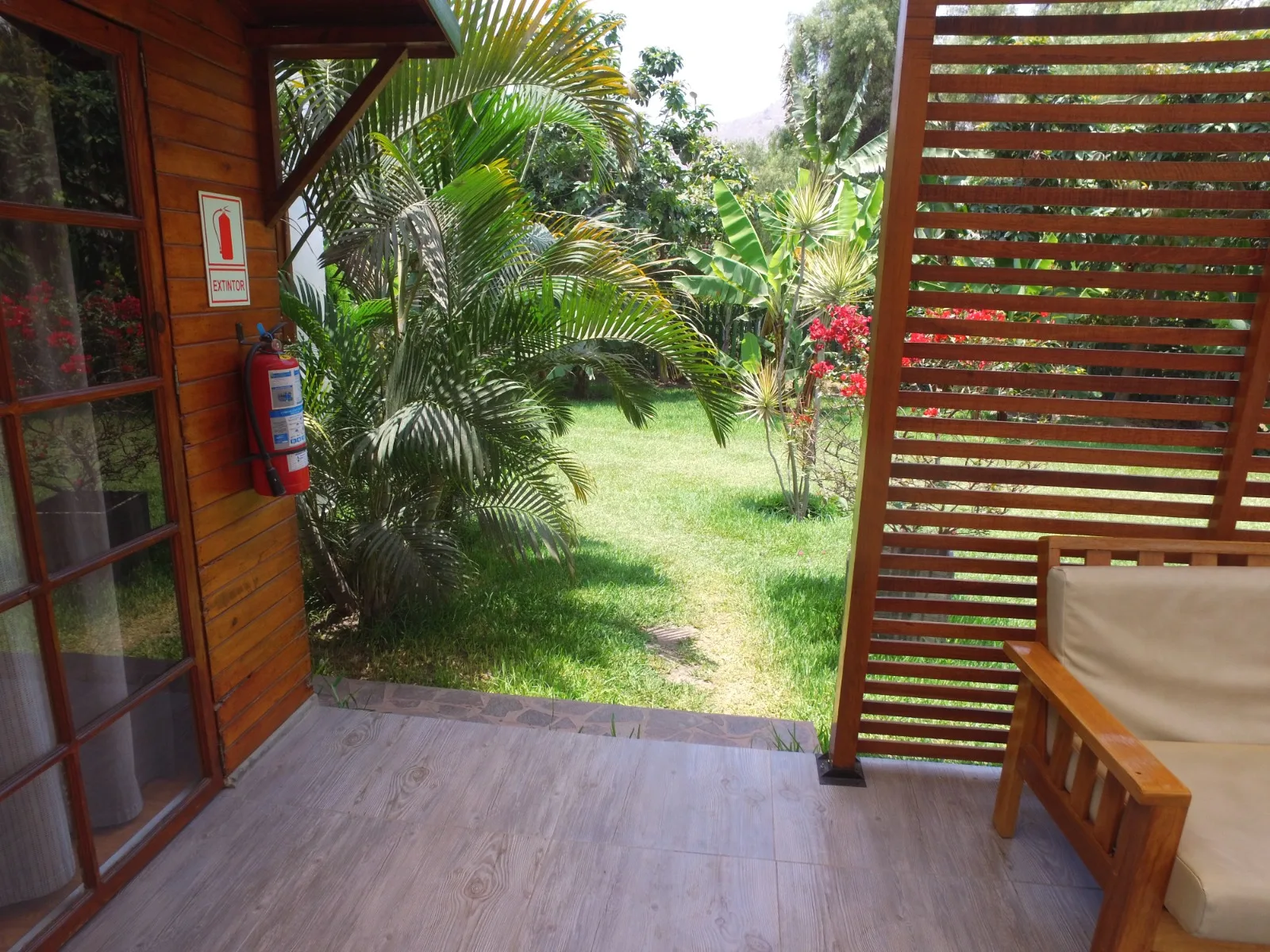 Pequeño patio exterior junto a una estructura de madera con una puerta de vidrio y un extintor de incendios en una casa en alquiler en Cieneguilla.