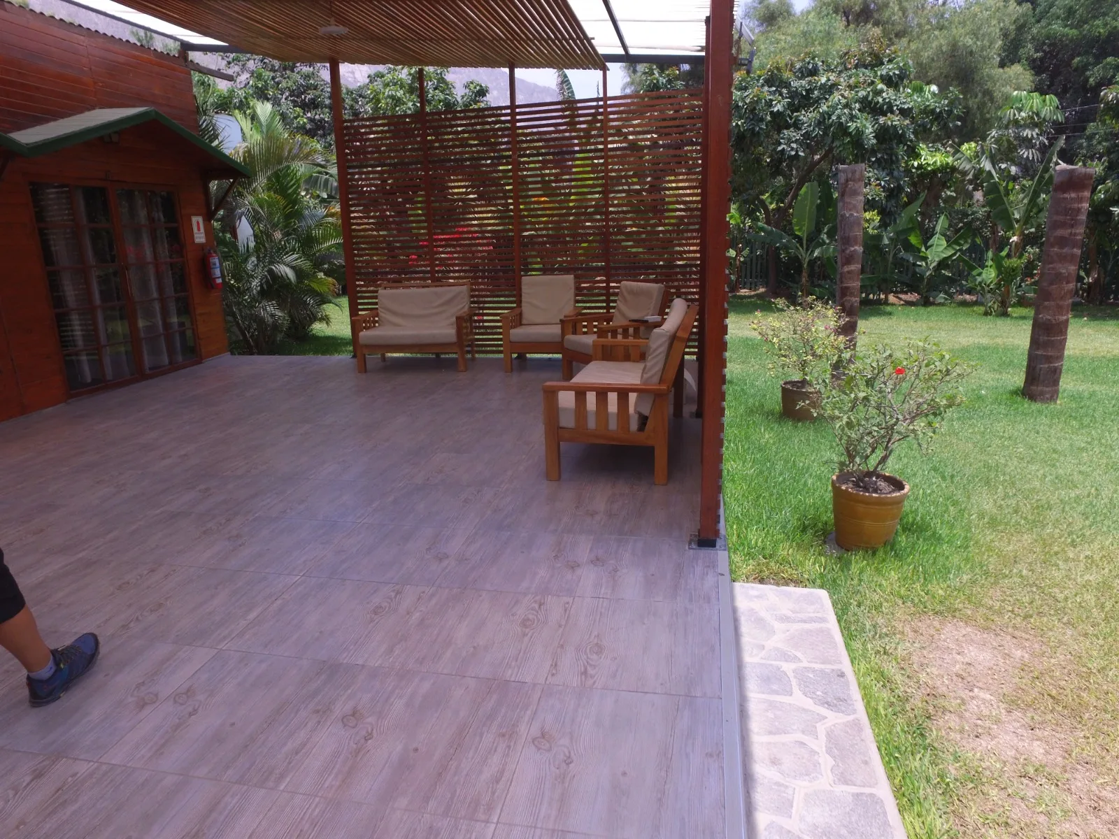 Patio exterior con estructura de madera, techo de listones y muebles de madera con cojines beige en una casa en alquiler en Cieneguilla.