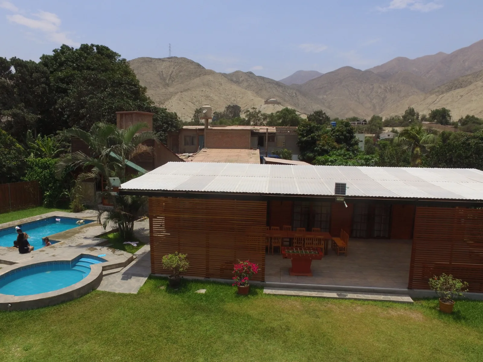 Patio trasero con piscina, jacuzzi, césped bien cuidado, mesas y sillas de madera en una casa en alquiler en Cieneguilla.