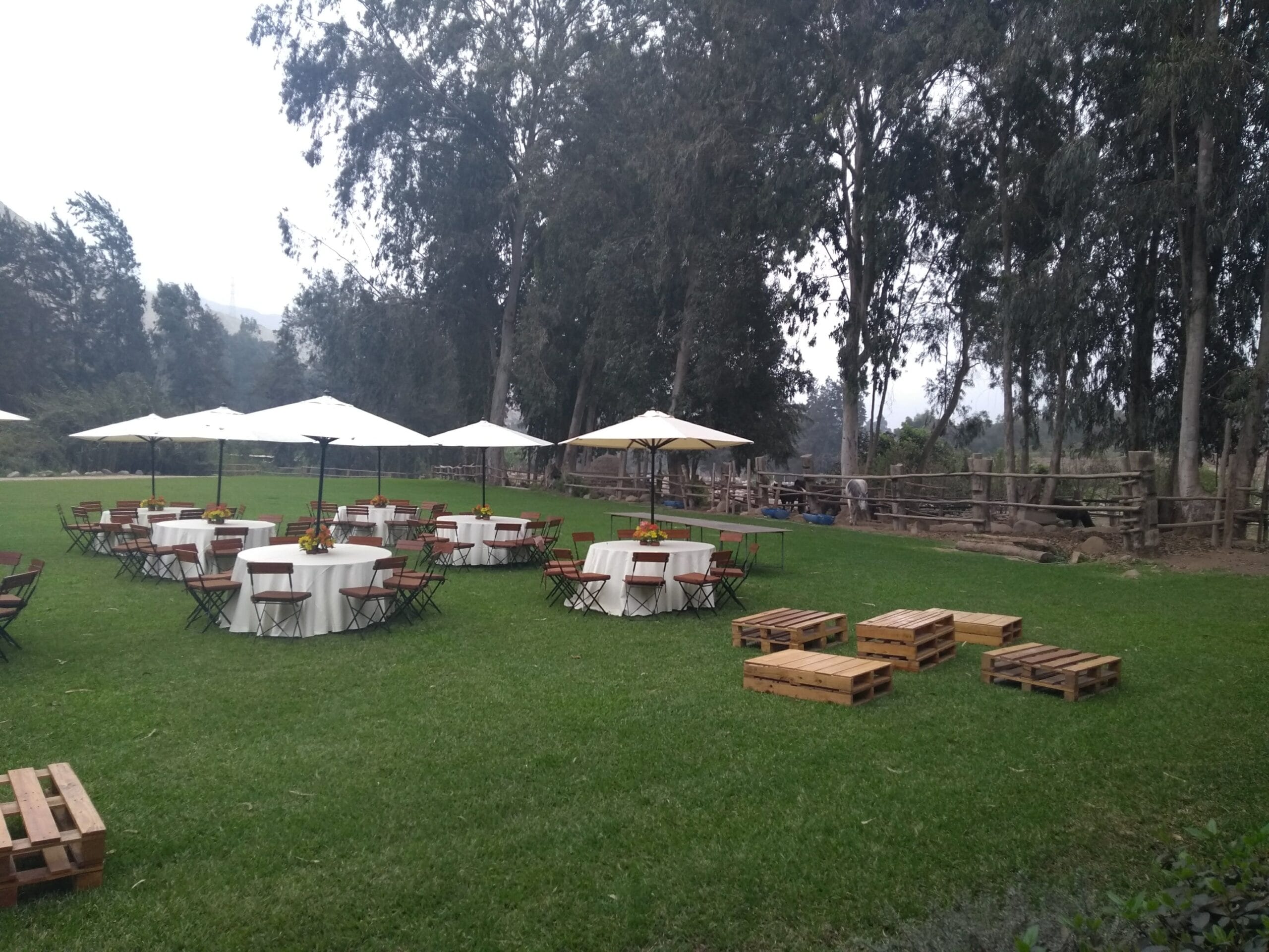 Evento al aire libre con mesas redondas, sombrillas blancas y jardín en Cieneguilla