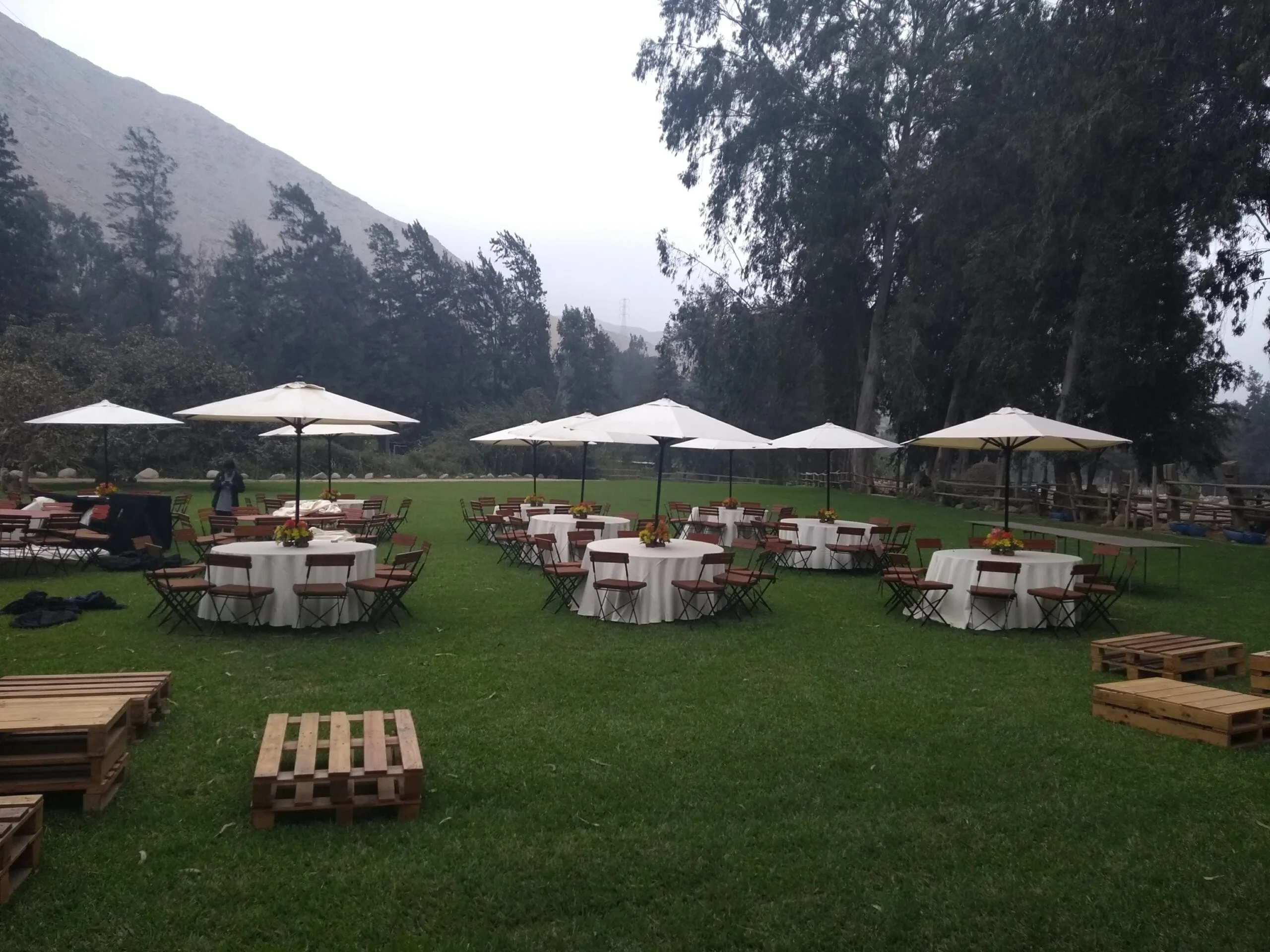 Evento al aire libre con mesas redondas, sombrillas blancas y jardín en Cieneguilla