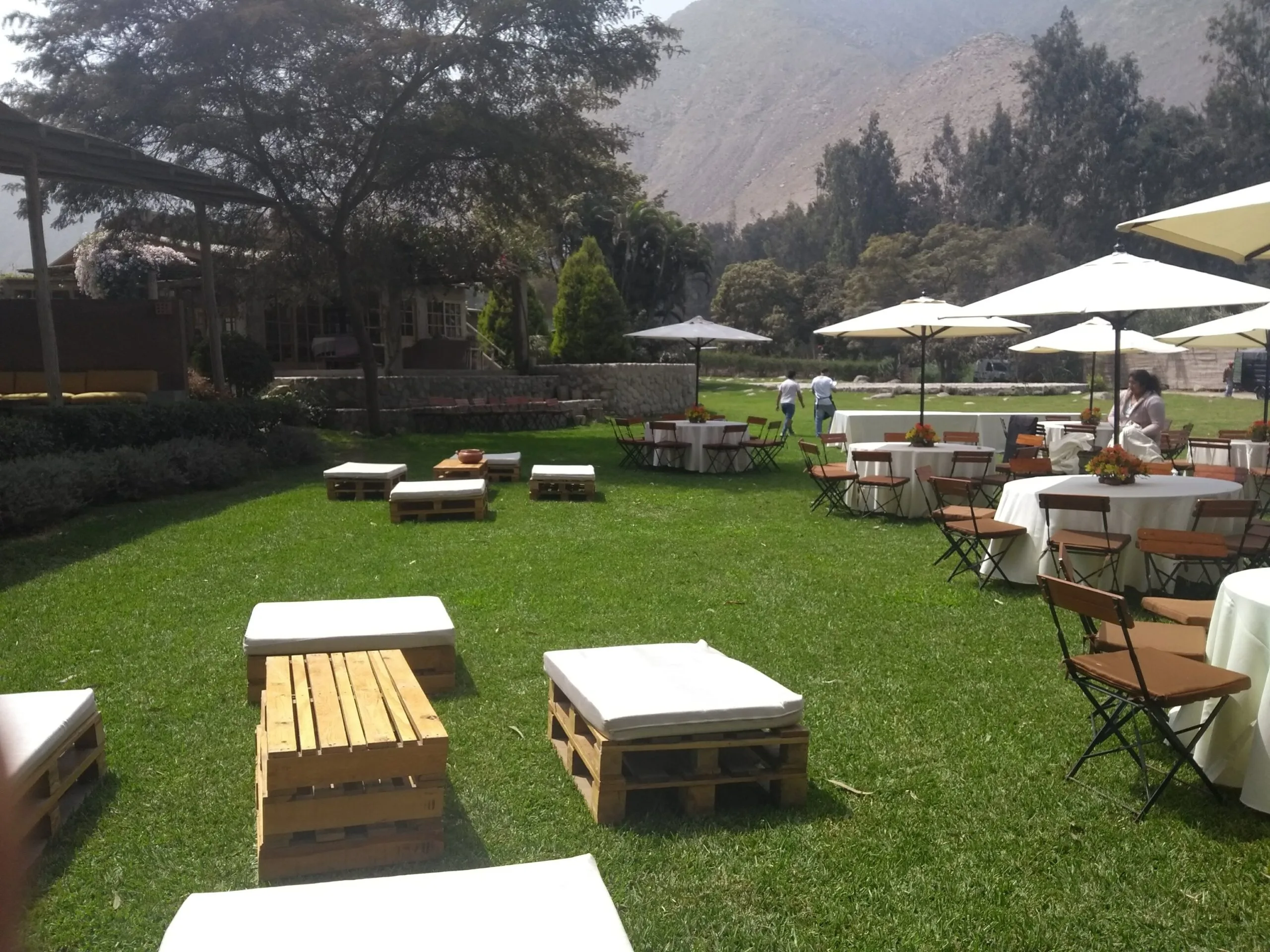 Evento al aire libre con mesas redondas, sombrillas blancas y jardín en Cieneguilla
