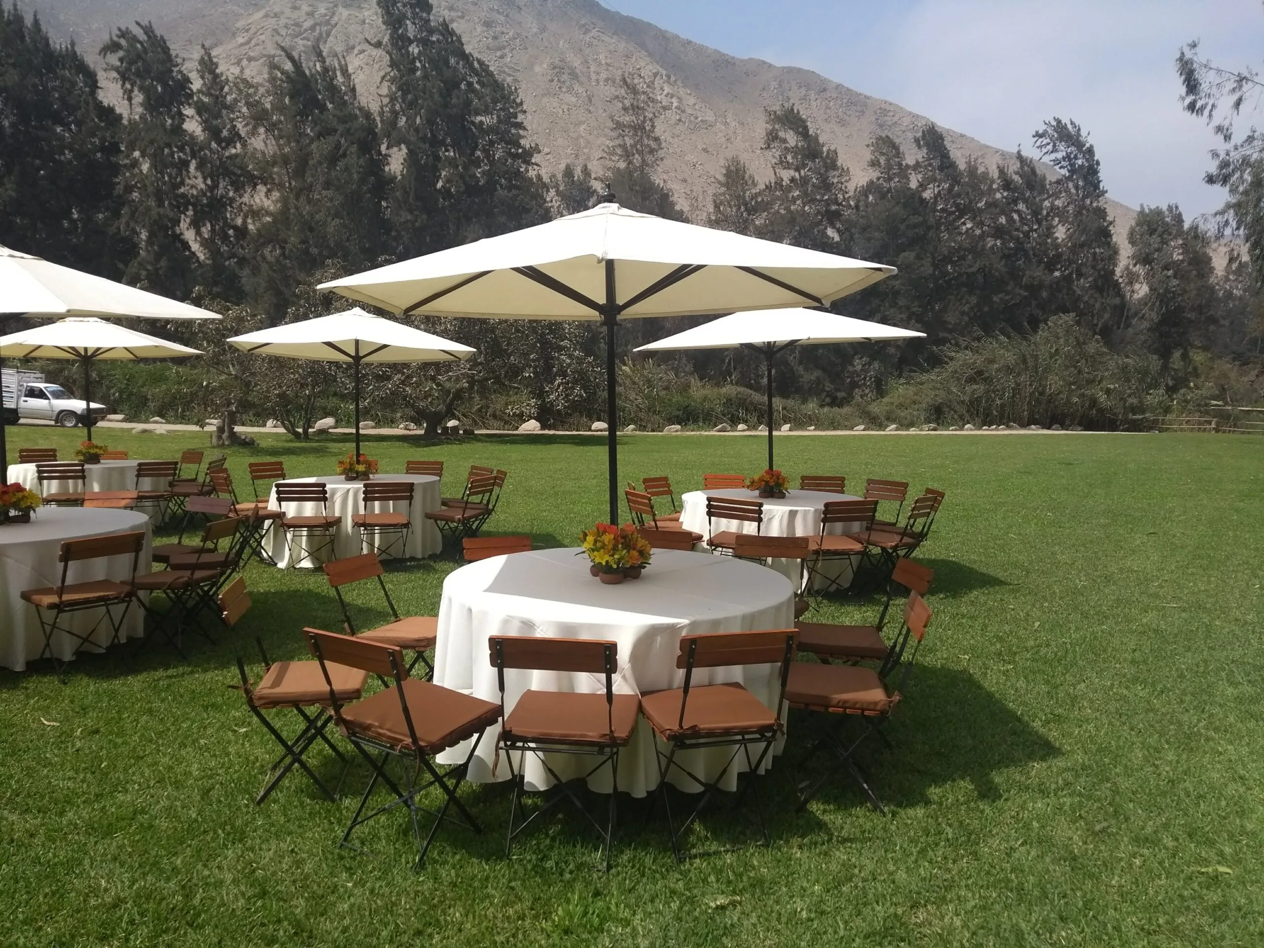 Evento al aire libre con mesas redondas, sombrillas blancas y jardín en Cieneguilla