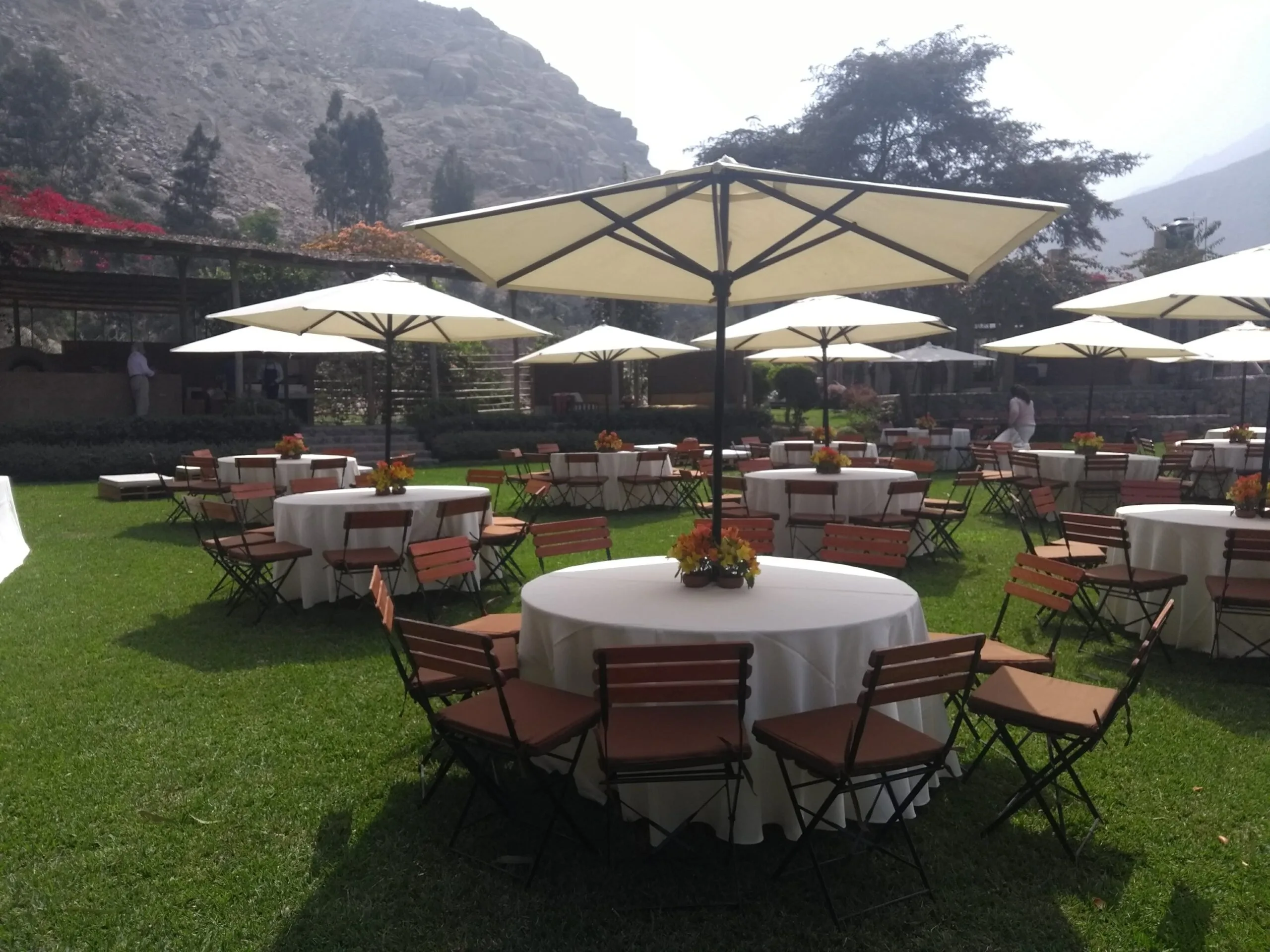 Evento al aire libre con mesas redondas, sombrillas blancas y jardín en Cieneguilla