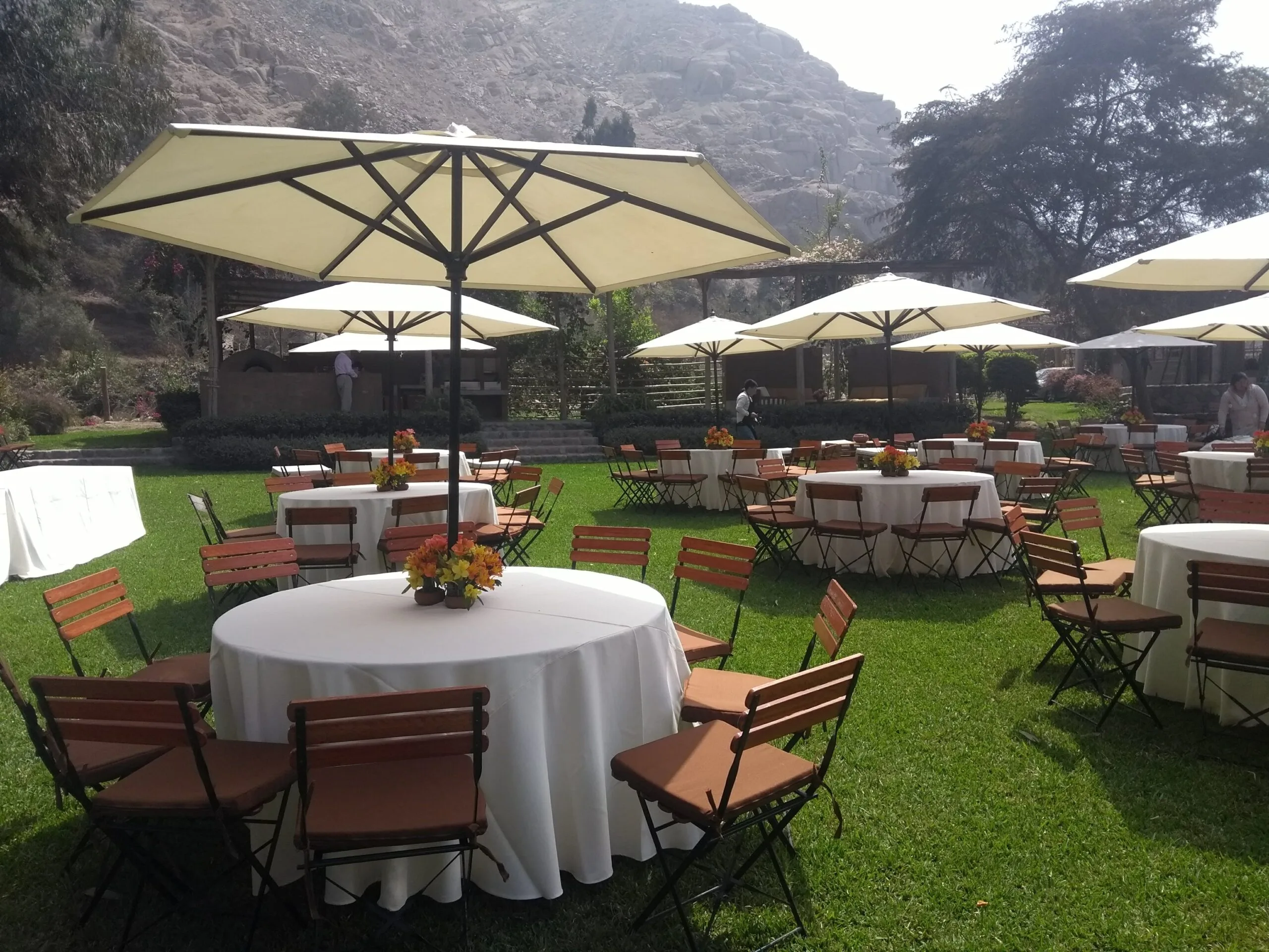 Evento al aire libre con mesas redondas, sombrillas blancas y jardín en Cieneguilla