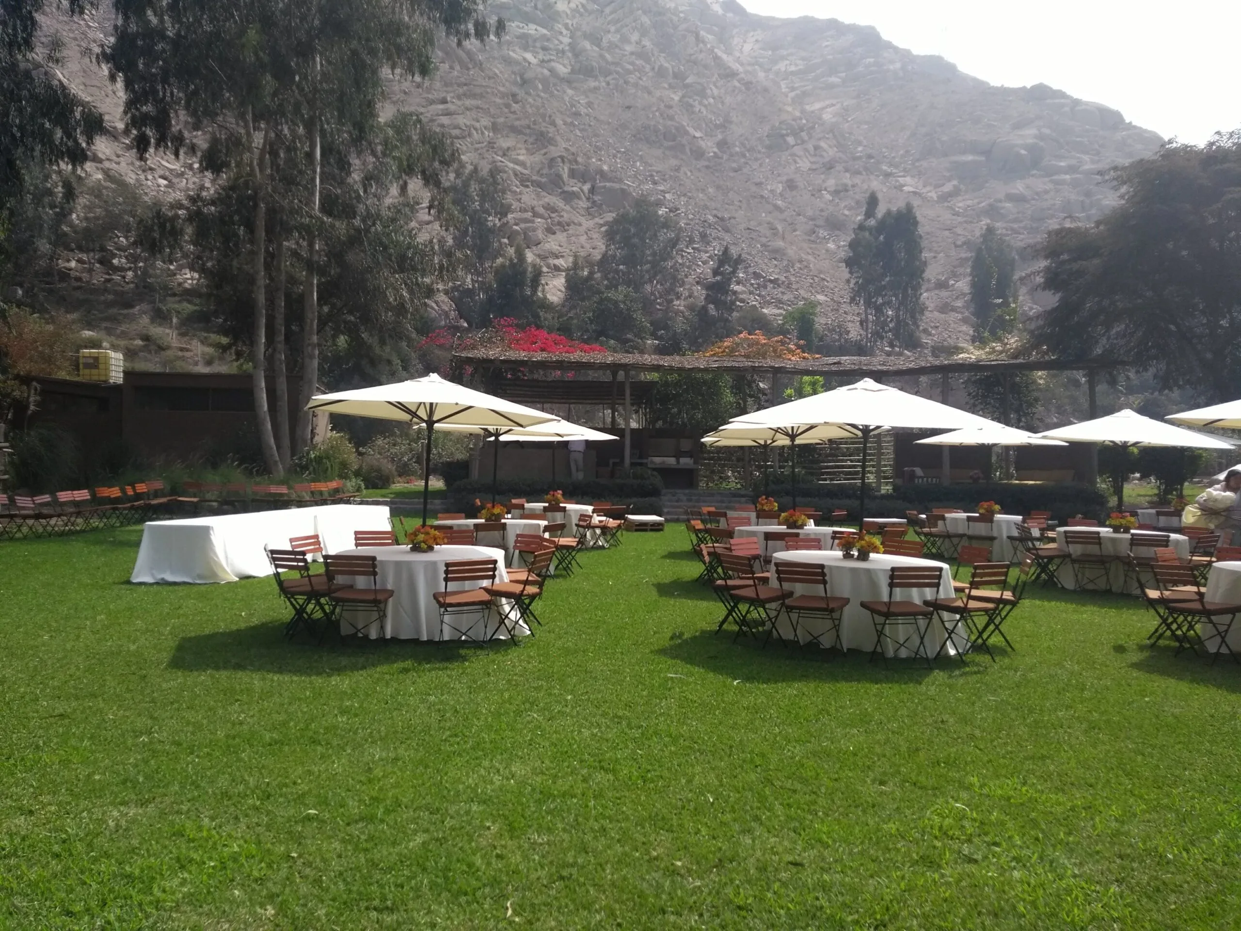 Evento al aire libre con mesas redondas, sombrillas blancas y jardín en Cieneguilla