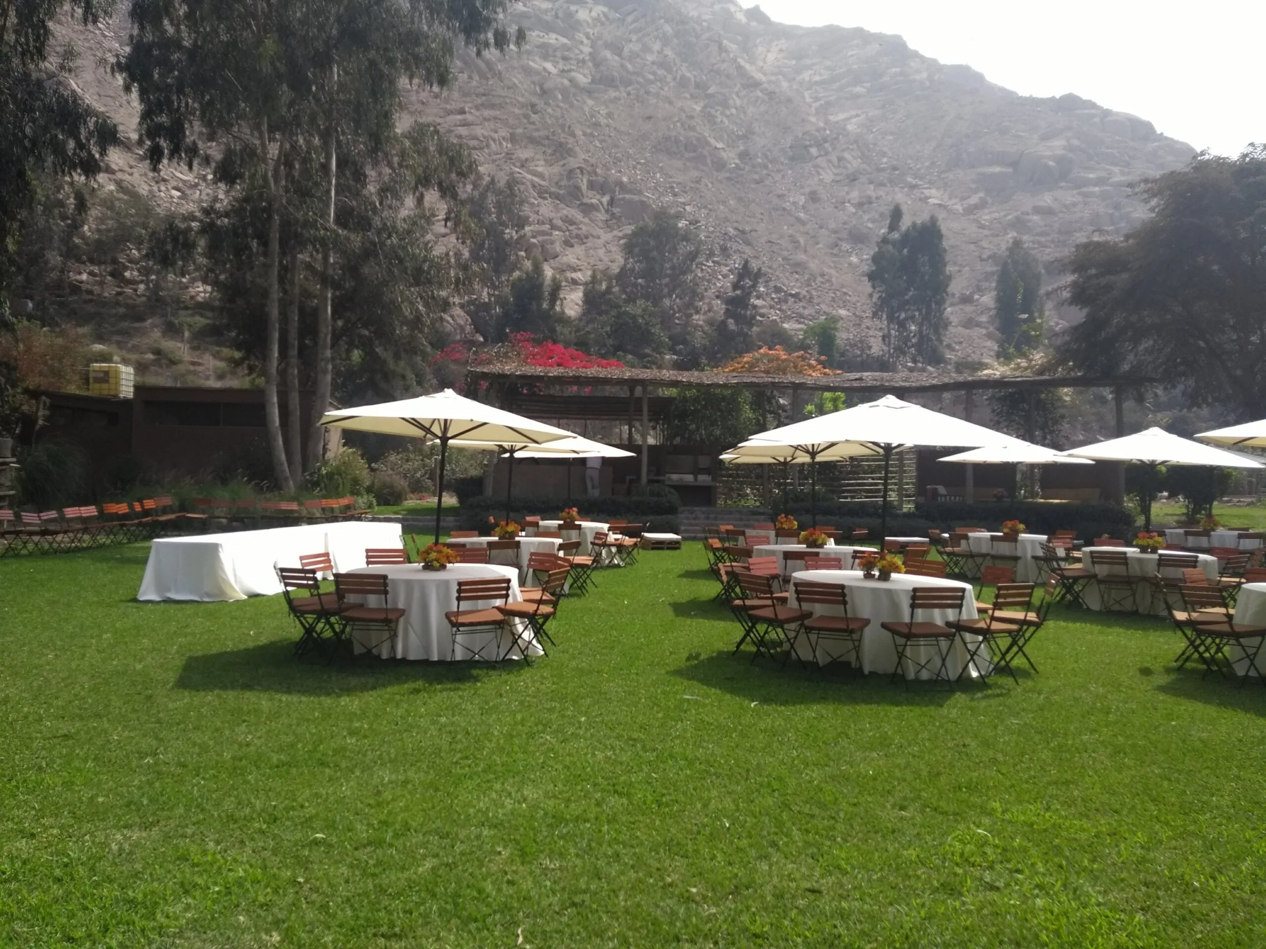 Evento al aire libre con mesas redondas, sombrillas blancas y jardín en Cieneguilla