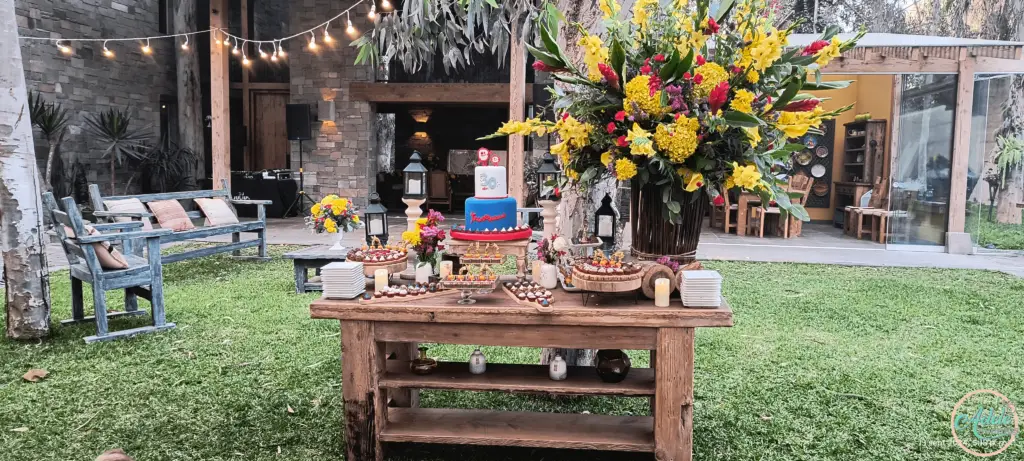 festejo-cumpleaños-30-exterior-decoracion-rustica-mesa-dulces-cieneguilla Mesa decorada para cumpleaños al aire libre con pastel de dos niveles y arreglos florales.