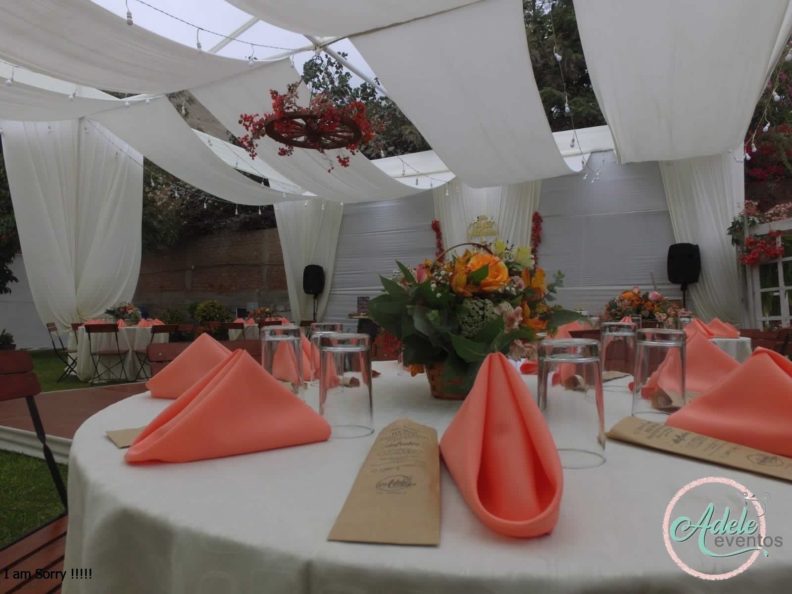 Mesas de boda elegantemente arregladas con manteles blancos, servilletas coral y centros de mesa florales en un evento al aire libre en Cieneguilla.