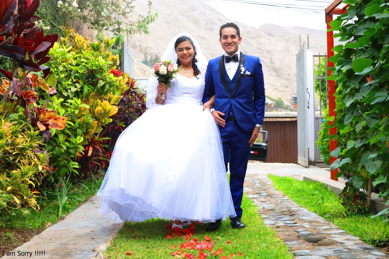 Pareja de novios caminando en un jardín en Cieneguilla durante su boda, con la novia en un vestido blanco y el novio en un traje azul.