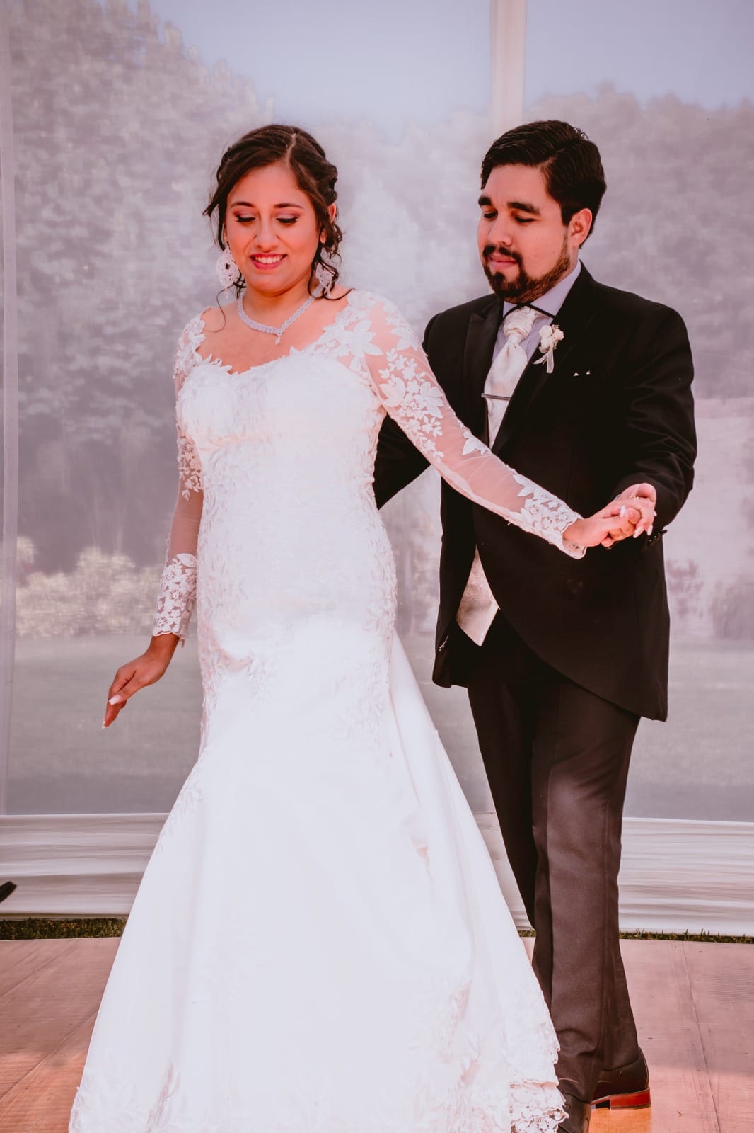 Pareja vestida formalmente, una con vestido de novia blanco y otra con traje oscuro, posiblemente bailando en su boda en Cieneguilla