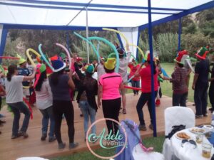 Colaboradores de una empresa bailando con sombreros festivos y globos bajo un toldo durante un evento de Adele Eventos en Cieneguilla.